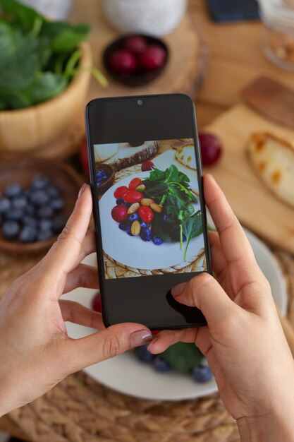 Persona que toma una foto de un plato de tomates, arándanos y espinacas con un teléfono inteligente