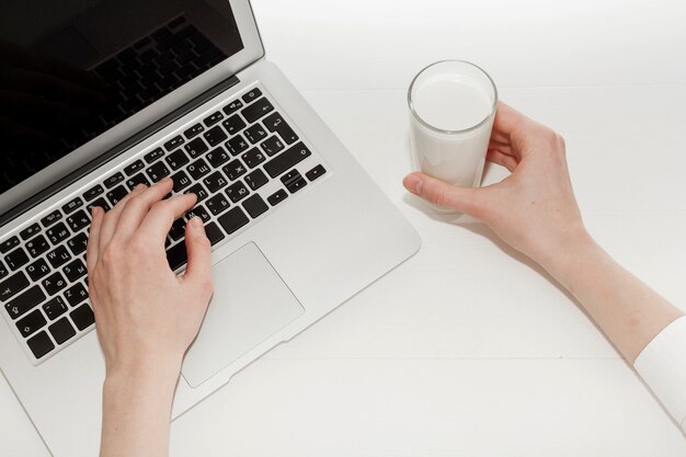 Persona que trabaja en la computadora portátil junto a un vaso de leche