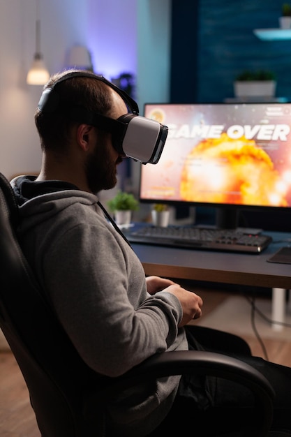 Persona que usa gafas vr para jugar videojuegos con controlador en la computadora. Hombre perdiendo el juego con gafas de realidad virtual y joystick frente al monitor. Jugador jugando videojuegos.