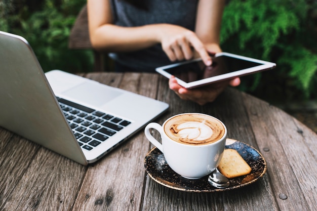 Persona que usa la tableta cerca de la computadora portátil y el café