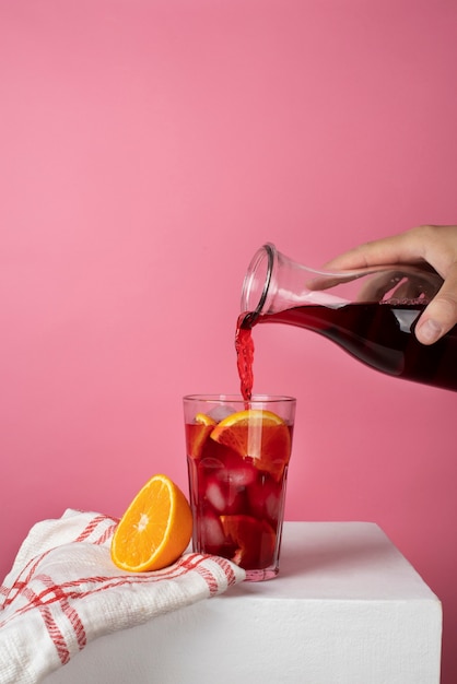 Foto gratuita persona que vierte refrescante té helado de hibisco en un recipiente de vidrio transparente