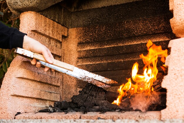 Una persona quema a mano carbón con tong en firepit