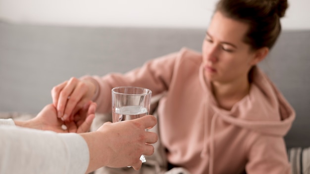 Foto gratuita persona de sexo femenino enferma que recibe agua y pastillas