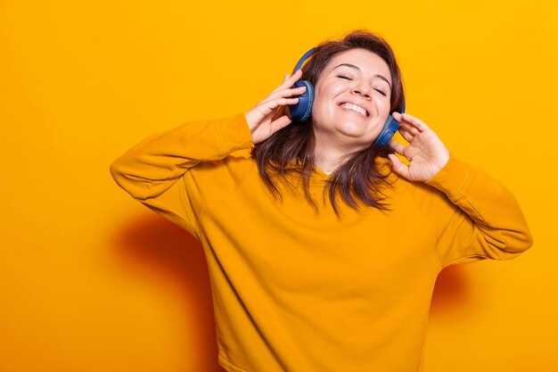 Persona sonriente que se siente feliz y escucha música, usando auriculares modernos en la cámara. Mujer con sonrisa con auriculares para escuchar canciones y audio para divertirse y entretenerse.