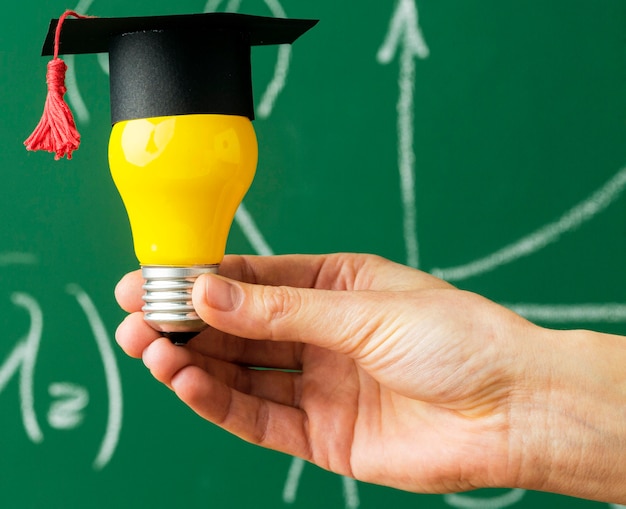 Persona sosteniendo bombilla con gorra académica