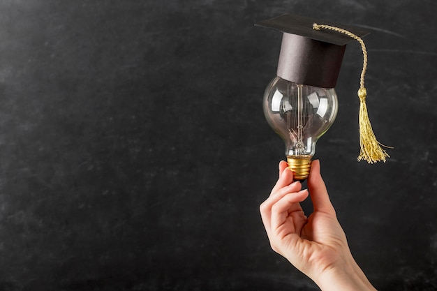 Foto gratuita persona sosteniendo una bombilla con gorro de graduación