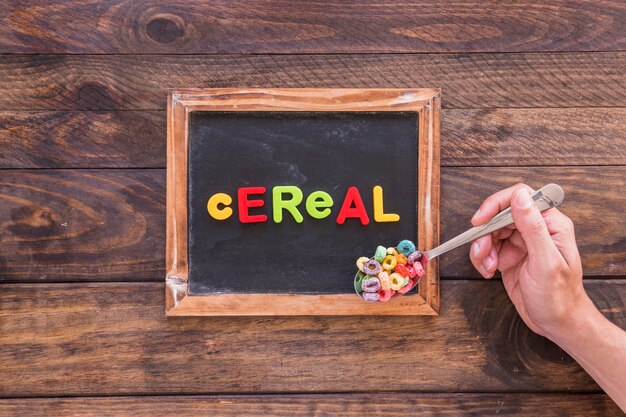 Persona sosteniendo una cuchara con cereal encima de pizarra