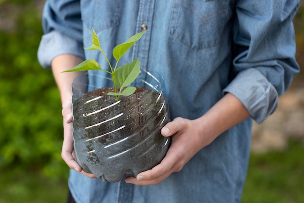 Persona sosteniendo una planta en una maceta de plástico