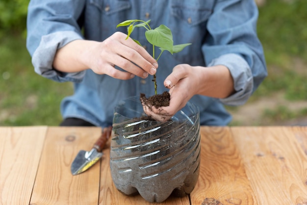 Persona sosteniendo una planta en una maceta de plástico