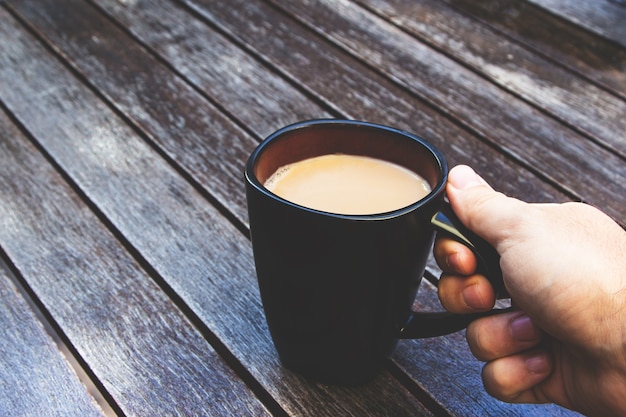 Persona sosteniendo su taza negra llena de café sobre una superficie de madera