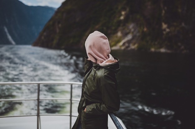 Persona con una sudadera con capucha de pie en el barco durante el crucero en Milford Sound en Nueva Zelanda