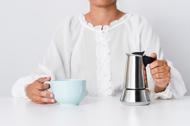 Persona con taza de cerámica y hervidor de agua