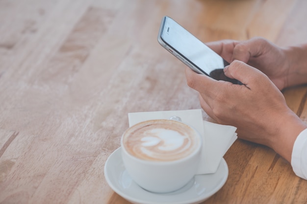 Persona con un teléfono inteligente y un café.