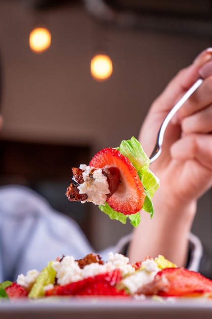 Persona con un tenedor sosteniendo parte de la ensalada de frutas y verduras