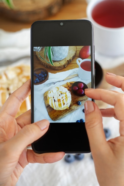 Persona tomando fotos de hojaldre y té con teléfono inteligente