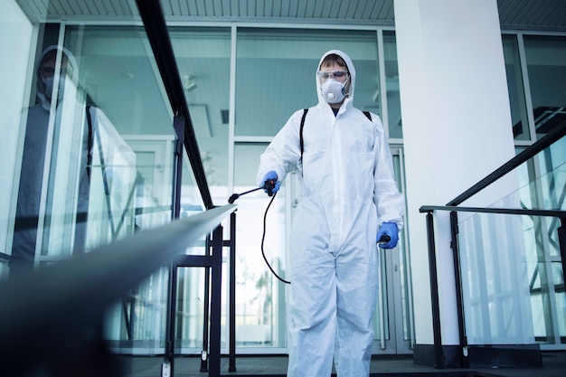 Persona con traje blanco de protección química que realiza la desinfección de áreas públicas para detener la propagación del virus corona altamente contagioso