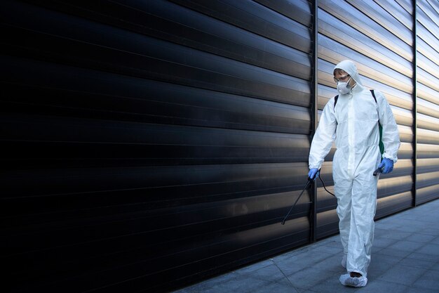 Persona con traje blanco de protección química realizando desinfección y control de plagas y rociando veneno para matar insectos y roedores