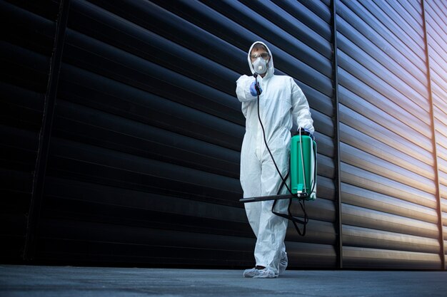 Persona con traje blanco de protección química realizando desinfección y control de plagas y rociando veneno para matar insectos y roedores