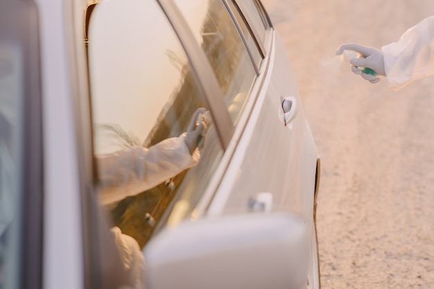 Persona en traje de protección desinfecta el auto