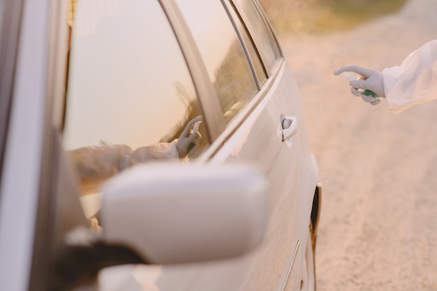 Persona en traje de protección desinfecta el auto