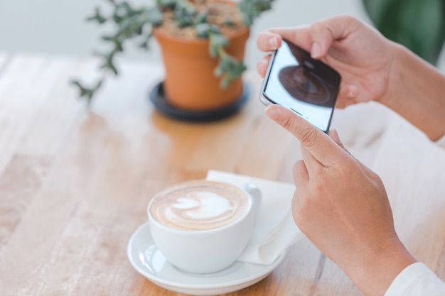 La persona usa una cámara de un teléfono inteligente para capturar una taza de café con leche