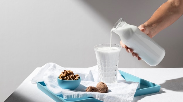 Persona vertiendo leche en vaso lleno con nueces en bandeja