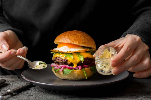 Persona de la vista frontal cerca de la hamburguesa en el plato que sostiene el frasco con mantequilla