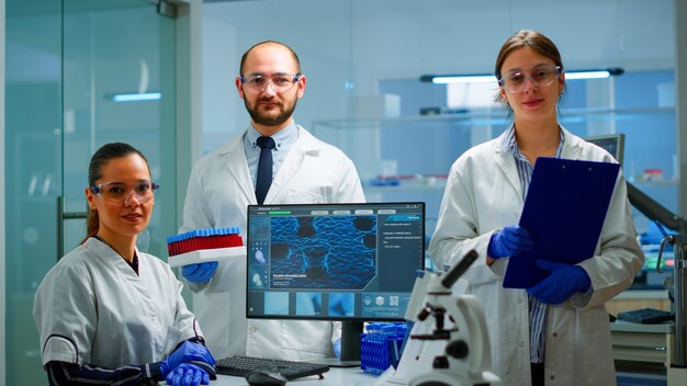 Personal médico científico profesional mirando a la cámara en un moderno laboratorio equipado. Equipo de médicos que examinan la evolución del virus con alta tecnología, herramientas químicas para la investigación científica y el desarrollo de vacunas.