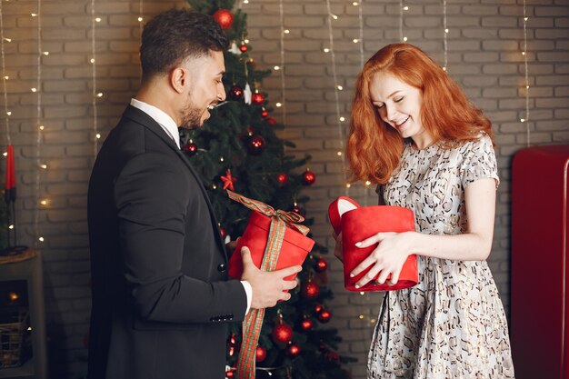 Personas en adornos navideños. Hombre con traje negro. Mujer con caja roja.