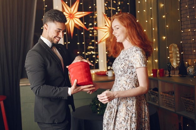 Personas en adornos navideños. Hombre con traje negro. Mujer con caja roja.