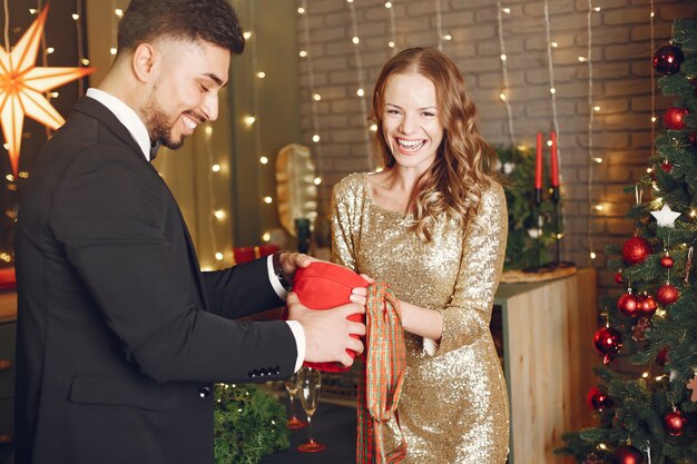 Personas en adornos navideños. Hombre con traje negro. Mujer con caja roja.