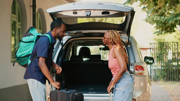 Personas casadas poniendo equipaje dentro del vehículo mientras van de viaje de campo. Pareja cargando equipaje de viaje y carros dentro del baúl del auto mientras se prepara para la salida de vacaciones en la ciudad