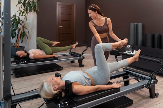 Foto gratuita personas en clase reformadora de pilates ejercitando sus cuerpos