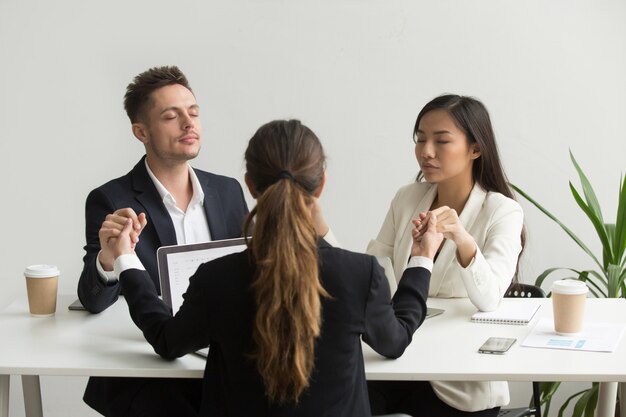 Personas conscientes del equipo diverso tomados de la mano meditando orando por el éxito