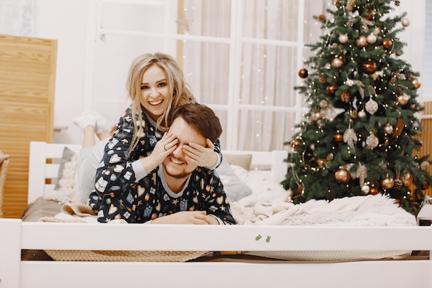 Personas en decoraciones de Christman. Hombre y mujer en pijama identifical. Familia en una cama.