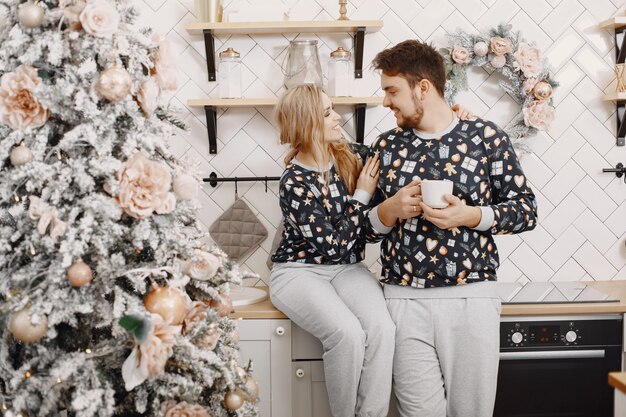 Personas en decoraciones de Christman. Hombre y mujer en pijama identifical. Familia en una cocina.