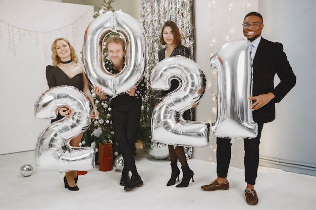 Foto gratuita personas en decoraciones de christman. hombre con traje negro. celebraciones grupales año nuevo. personas con globos 2021.