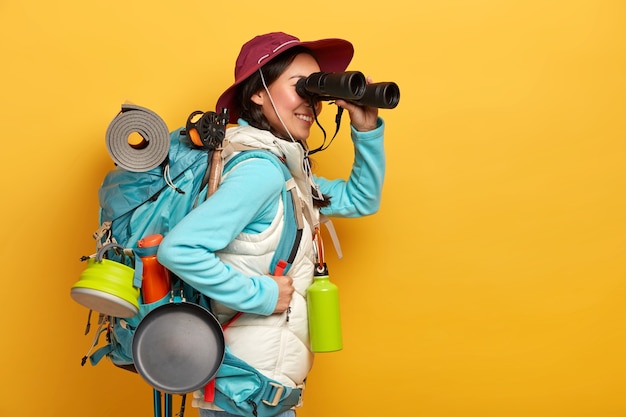 Personas, estilo de vida, vacaciones, concepto de turismo. Turista alegre observa algo en binoculares, se para con mochila, usa ropa deportiva casual