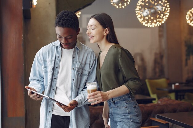 Personas internacionales de pie en una cafetería con tableta y café.