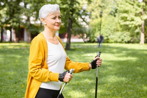 Personas maduras, envejecimiento, deportes y concepto de bienestar. Hermosa anciana elegante eligiendo un estilo de vida activo y saludable en la jubilación, pasar la mañana al aire libre, disfrutar de paseos escandinavos