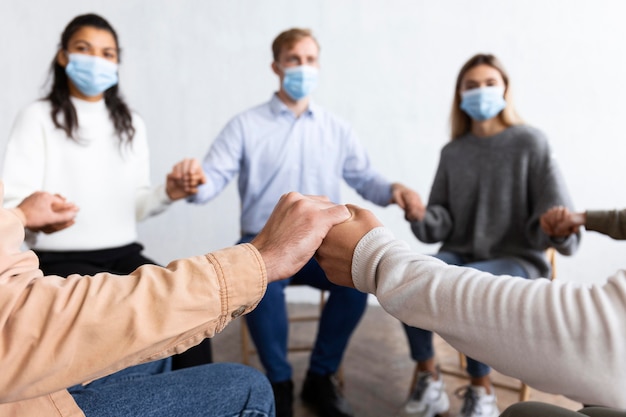 Personas con máscaras médicas tomados de la mano en la sesión de terapia de grupo