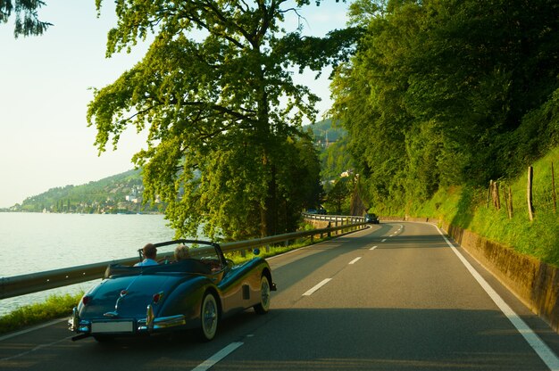 Personas mayores en el coche retro en la carretera con un hermoso paisaje de verano. Suizo.