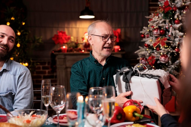 Las personas mayores ofrecen regalos en Navidad difundiendo la positividad y el espíritu navideño en las vacaciones de invierno en casa Una feliz pareja de ancianos celebra el evento estacional de diciembre con adornos festivos