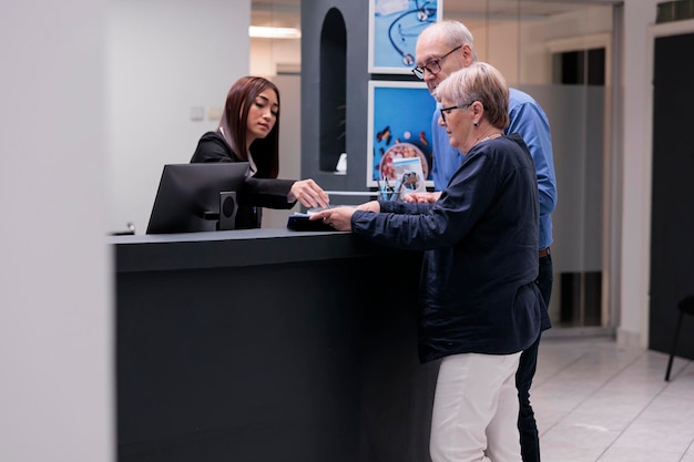 Personas mayores que escriben informes médicos con recepcionista antes de la cita de control con el médico en el centro de salud. Pacientes antiguos que firman formularios de registro y archivos, soporte de seguros.