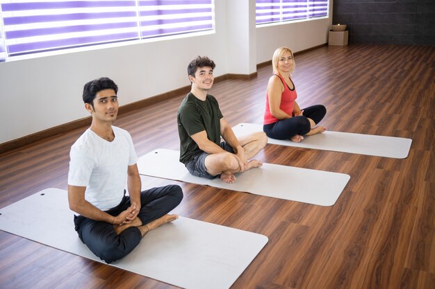 Personas positivas sentadas en colchonetas en clase de yoga