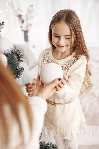 Personas que se preparan para la navidad. madre jugando con su hija. árbol de navidad decorado familiar. niña con un vestido blanco.