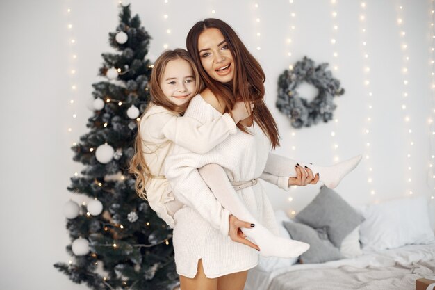 Personas que se preparan para la Navidad. Madre jugando con su hija. La familia está descansando en una sala festiva. Niña con un vestido blanco.