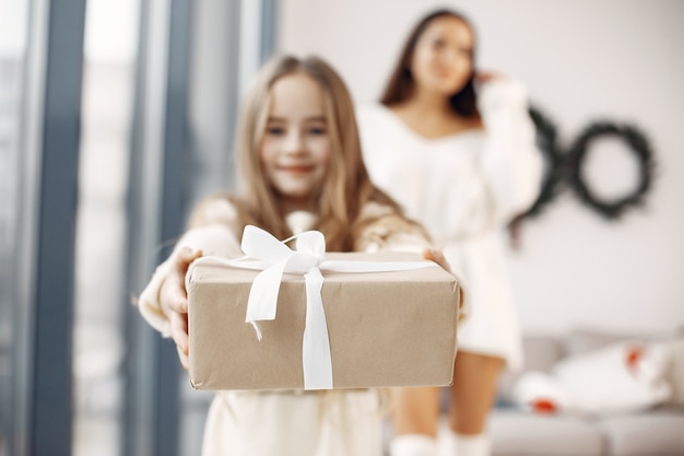 Personas que se preparan para la Navidad. Madre jugando con su hija. La familia está descansando en una sala festiva. Niña con un vestido blanco.