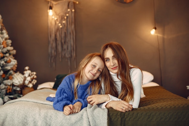 Personas que se preparan para Navidad. Madre jugando con su hija. La familia está descansando en una sala festiva. Niño con un suéter azul.