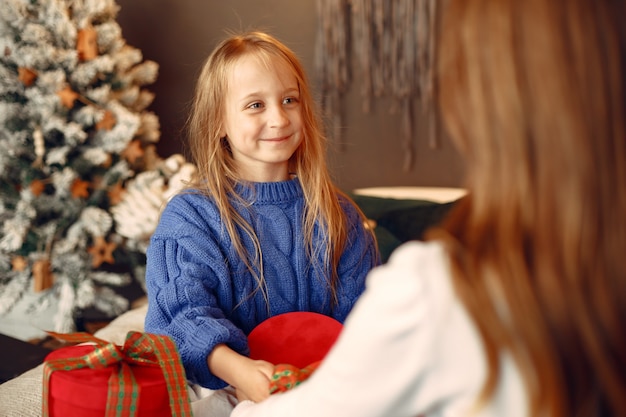 Personas que se preparan para Navidad. Madre jugando con su hija. La familia está descansando en una sala festiva. Niño con un suéter azul.